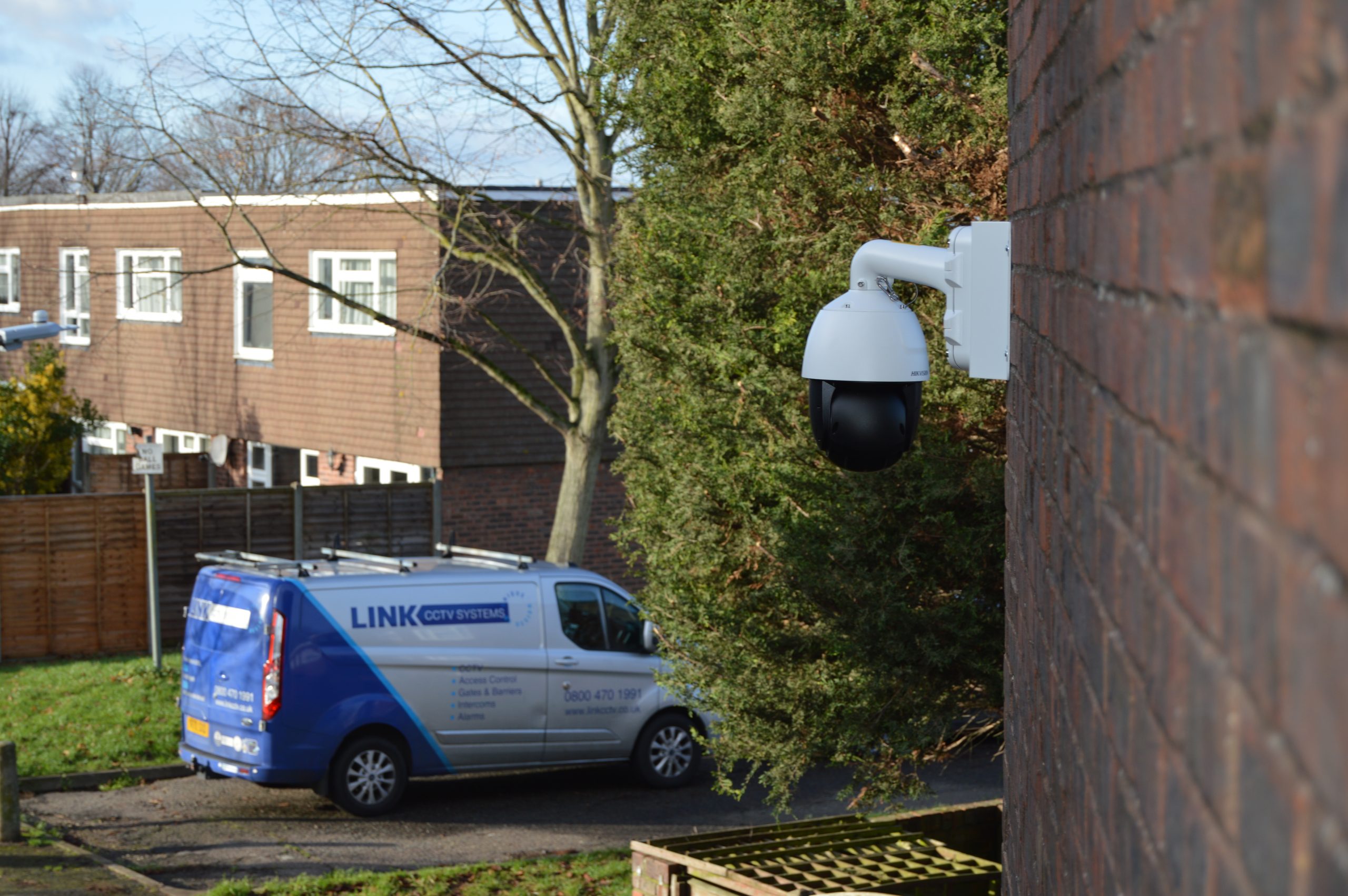 A camera installed on a brick wall by Link CCTV Systems, with a Link CCTV Systems van in the background.